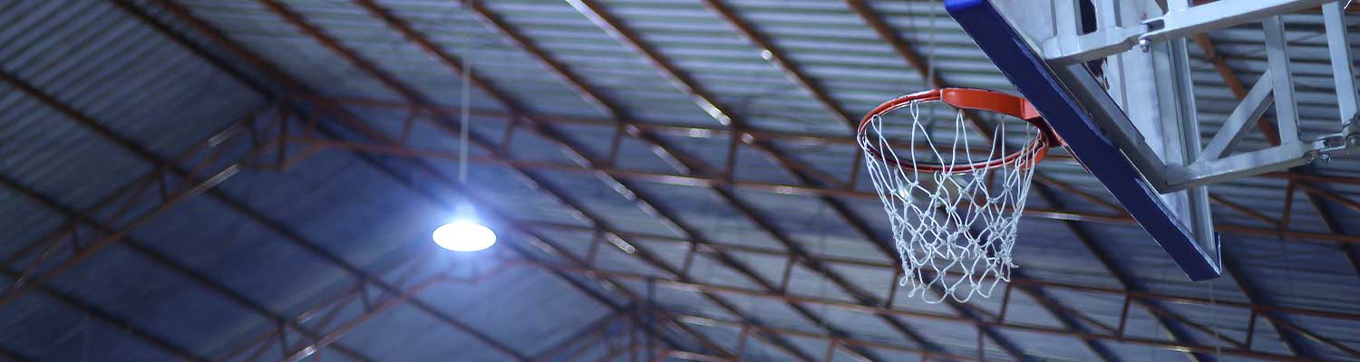 Key-Visual_Applications_Sports_and_Leisure_Facilities_Page Indoor basketball hoop mounted to a metal backboard, set against the high ceiling of a sports and leisure facility with exposed beams and bright overhead lighting
