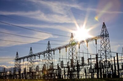 Puesta de sol detrás de una extensa subestación eléctrica con múltiples torres de alta tensión y líneas eléctricas, ilustrativa de la industria energética.
