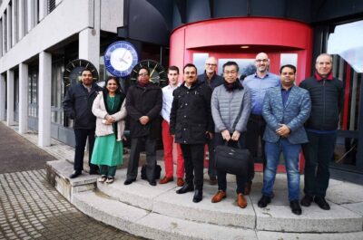 Délégation de haut niveau représentant les responsables du métro de Dhaka à Sumiswald avec les membres de l'équipe MOBATIME devant le bâtiment MOBATIME, horloges analogiques derrière à gauche.
